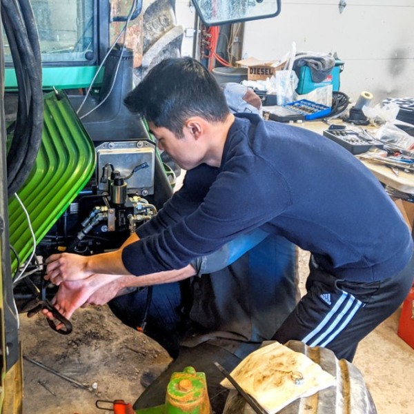 A male student working on a green tractor