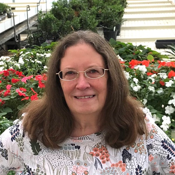 A headshot of a woman with glasses standing in front of flowers