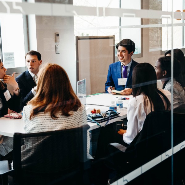 Male and female students sitting in a room at a table talking to one another