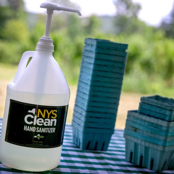 A large pump bottle of hand sanitizer on a table next to green cardboard blueberry boxes 