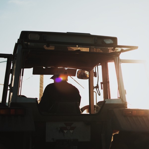 a person sitting in a tractor in a field with the sun setting behind him