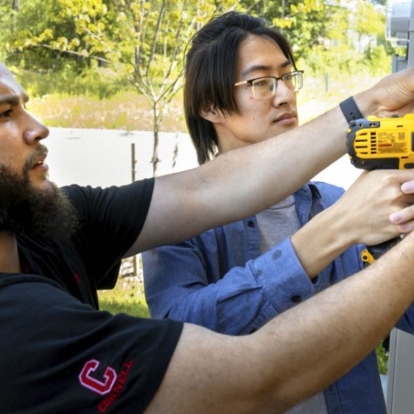 Two men drilling technology into the side of a house 
