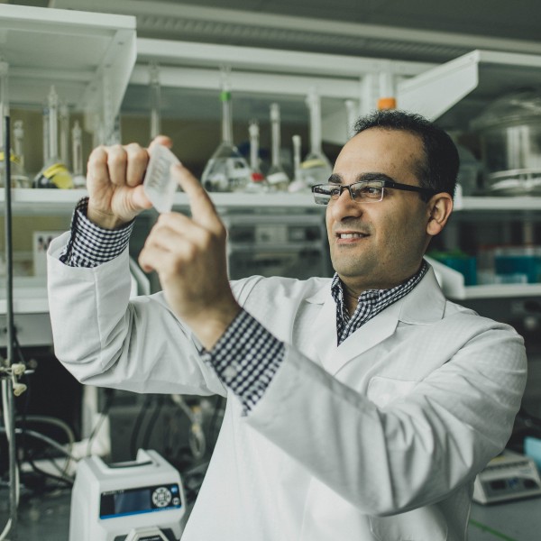 A man in a lab coat holds a slide up to the light.