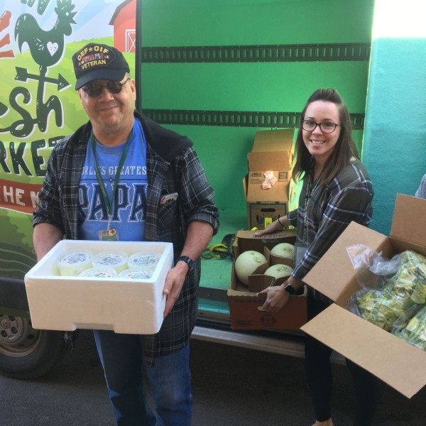 three volunteers show delivery boxes with dairy, melons, and greens