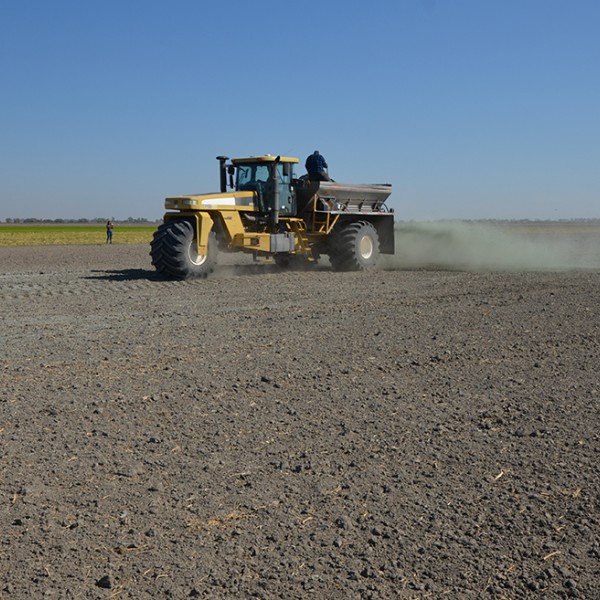 a tractor sprinkles rock dust over a tilled farm field