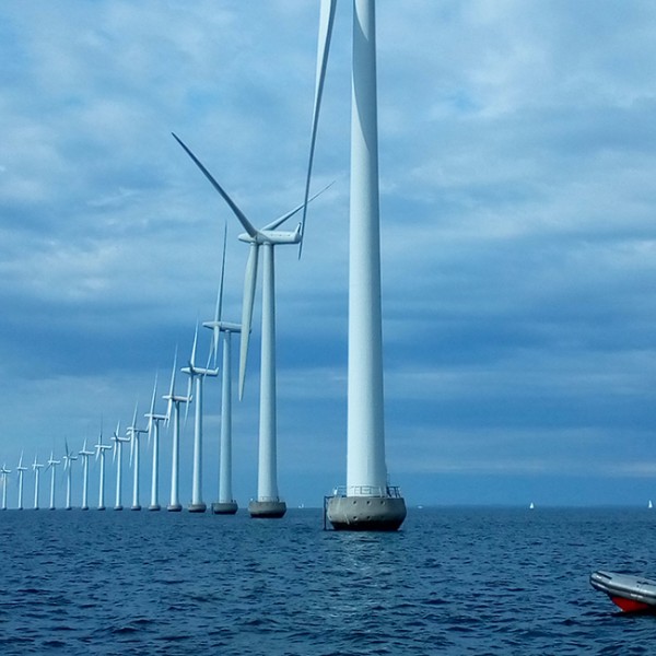 large wind turbines in the middle of the ocean with a boat floating nearby