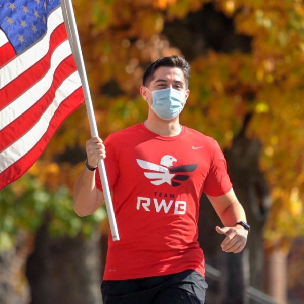 A man running outside while holding an American flag and wearing a mask