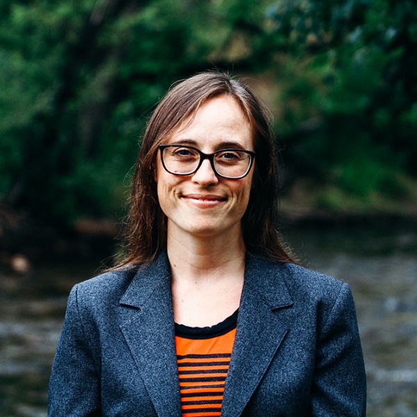 Angeline Pendergrass standing outside with water and green trees behind her