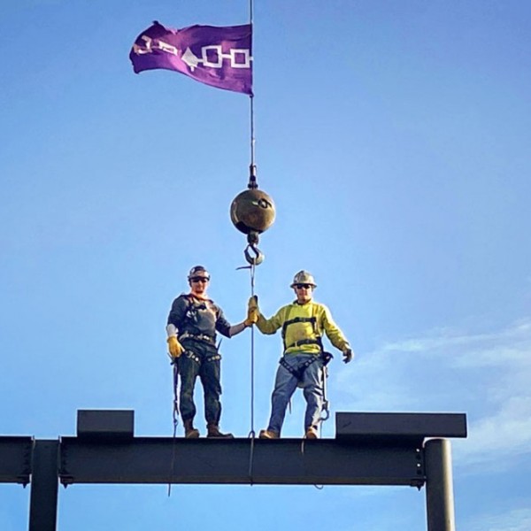 Two men stand on a construction scaffold flying a purple flag