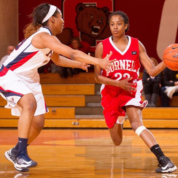 A female basketball player tries to dribble around an opponent