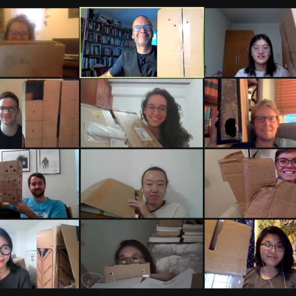 Male and female students sitting on a Zoom call holding up cardboard boxes 