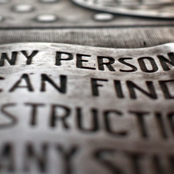 A silver Cornell Seal embedded in pavement that reads "Any person, any study"
