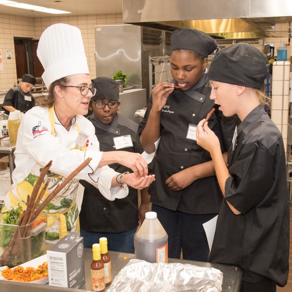three students and a chef in a school kitchen tasting recipes