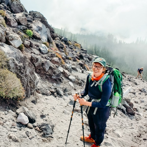 Ginny Moore hiking outside up a mountain carrying hiking poles and wearing a hate and backpack