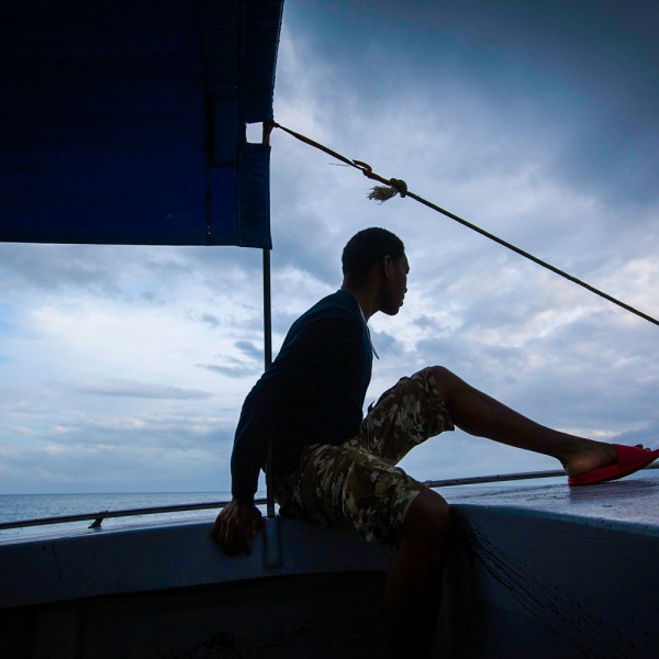 A person in silhouette at the front of a boat with a sail behind