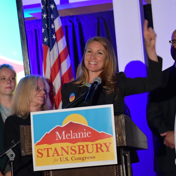 Melanie Stansbury celebrates with supporters on stage behind a podium with her campaign logo along