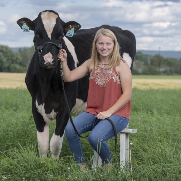 Rachel sitting on a stool outside holding onto a cow's bridal