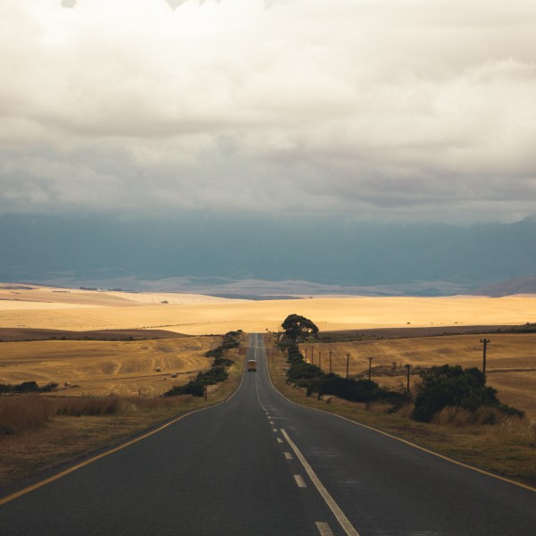 A school bus driving up a road in a very rural setting surrounded by fields
