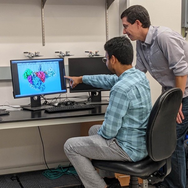 Chris Fromme and Saket Bagde gather around several computer monitors looking at the structure of a polyketide synthase enzyme