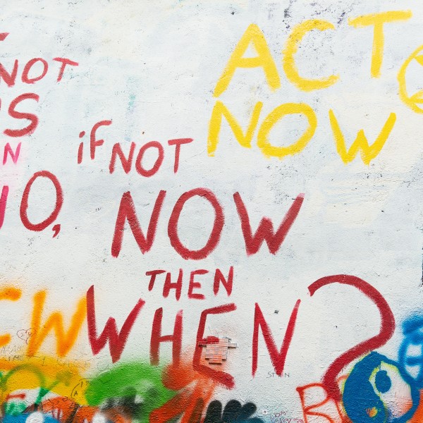 Graffiti on a white wall that says "If not us then who, if not now, then when?"