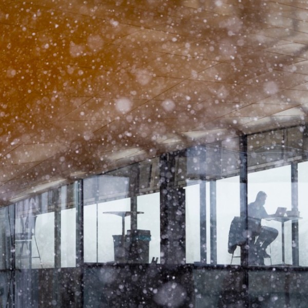 A person sitting at a table in Gates Hall while it snows outside