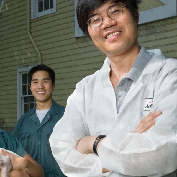 Xingen Lei standing with students outside. One student holds a piglet 