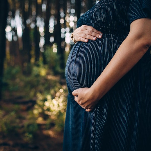 A woman standing in the woods holding her pregnant stomach 