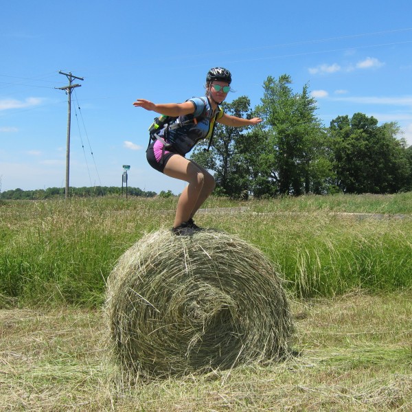 Girl in bike gear stands on top of hay