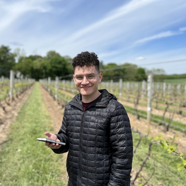 Male student poses with mobile device in vineyard.