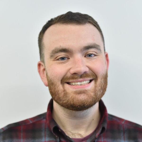 Portrait of Jacob Pucci. Man wearing red and gray plaid shirt with short brown hair. 