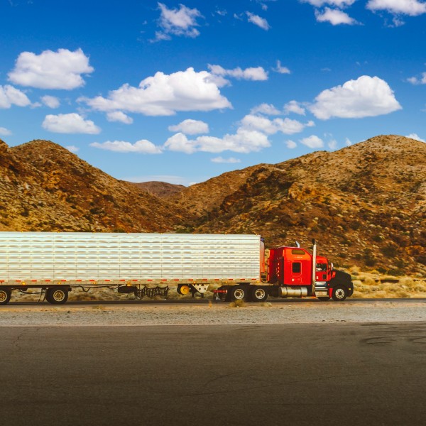 A 16-wheeler truck drives along a highway with mountains behind it 