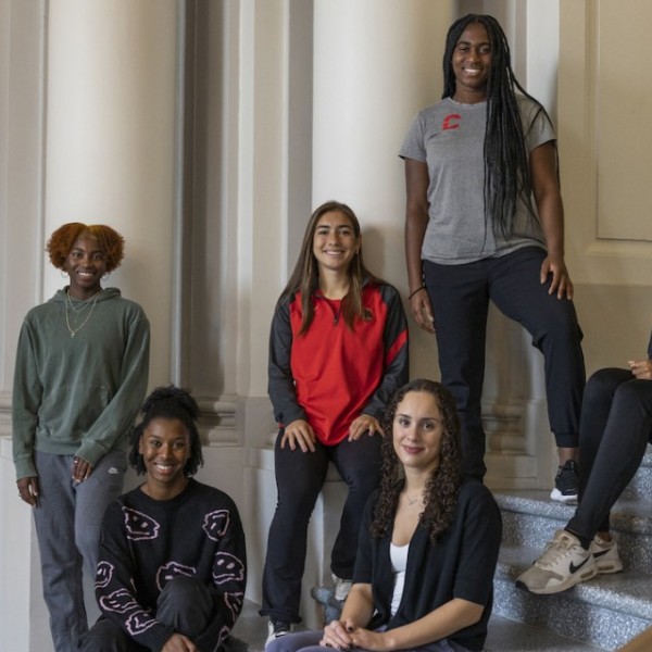 Group of six women sitting on the steps inside of Goldwin Smith Hall.