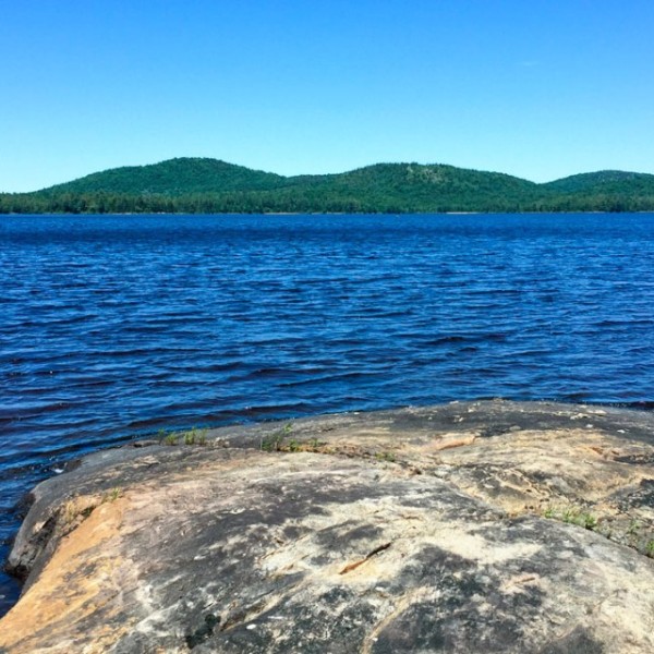 A photo of Lake Lila with a rock in the foreground with a hill in the background.