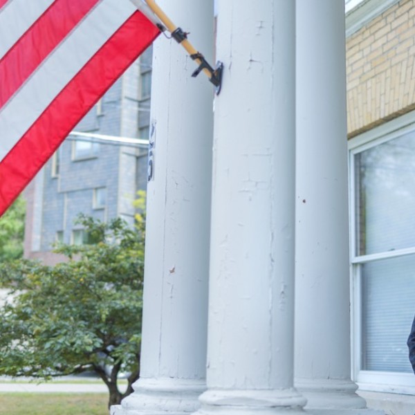 Andy Shin sitting outside of a building with the American flag flying behind him