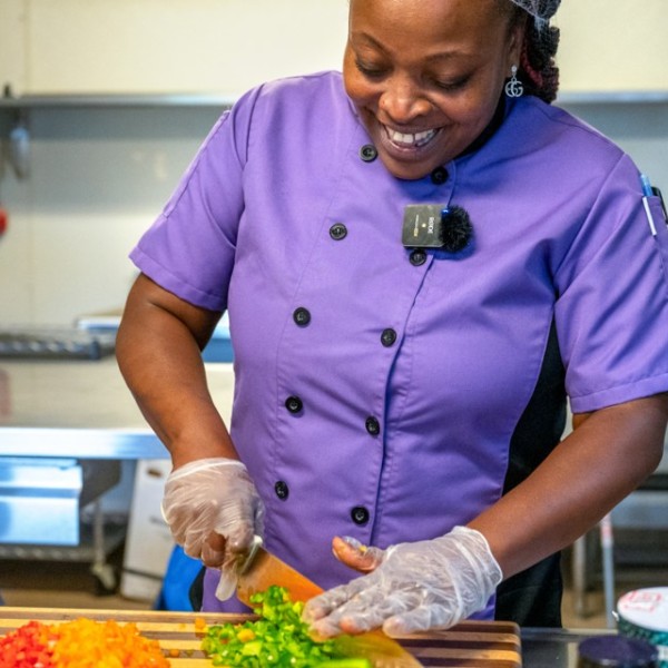 A woman chops vegetables while smiling.