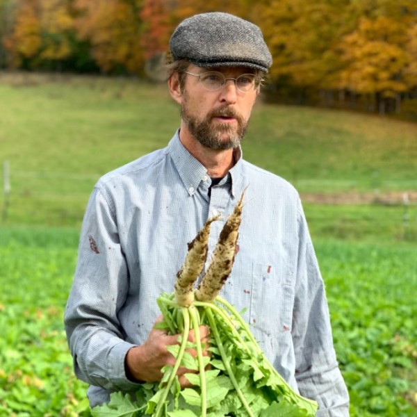 A man stands in a green field with two root vegetables in his hand.