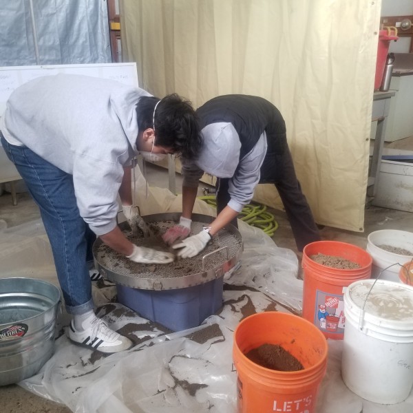 Two people mixing soil samples in buckets.