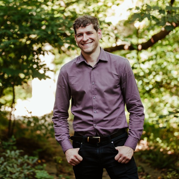Dan Katz stands in front of a background of green trees.