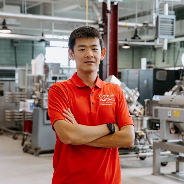 Chang Chen wearing a red polo shirt stands with arms folded in a food science lab.
