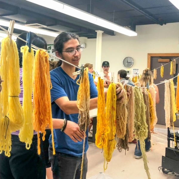 A male student adjusts yarn on a line drying.