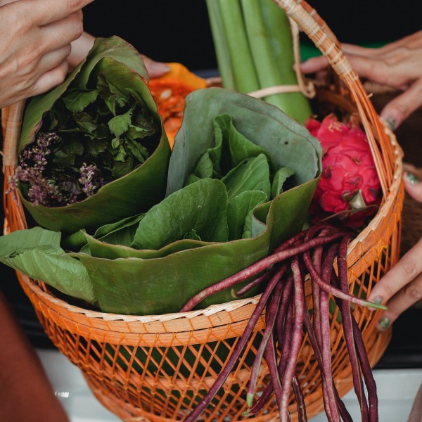 A basket of vegetables passed between two people. 