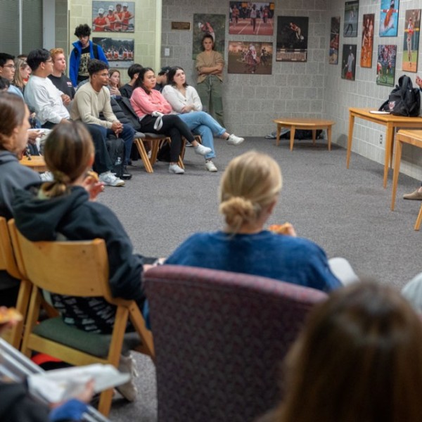 Students are seated in a half circle listening to a speaker.