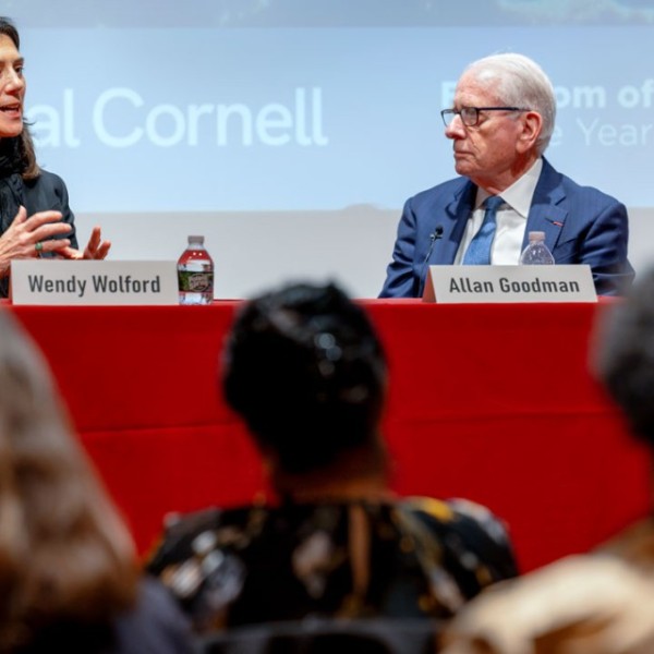 A man and a woman talk on a stage at a red table with "global cornell" and "freedom of expression" written on the wall behind them.