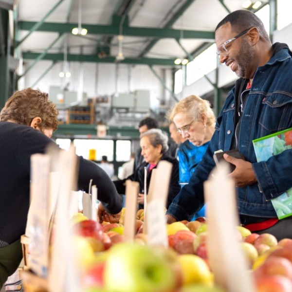 A man smiles while examining apples at a market.