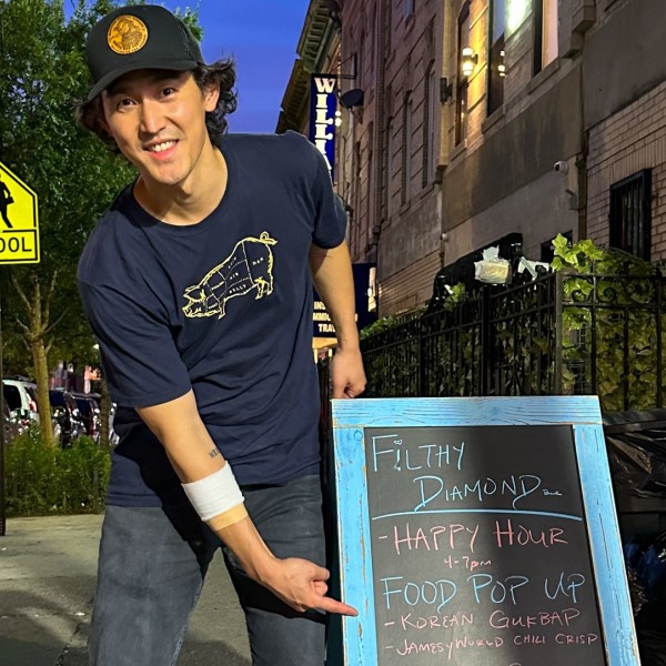 A man posing next to an A-frame chalkboard sign on the street.