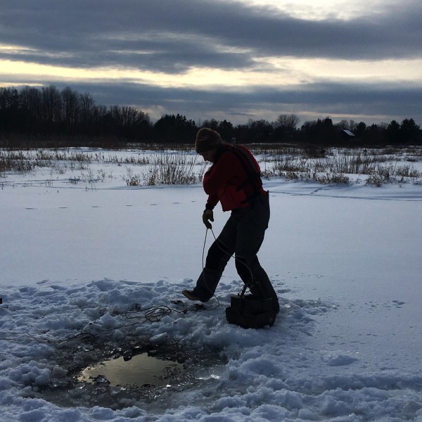 a woman drills into an iced over lake
