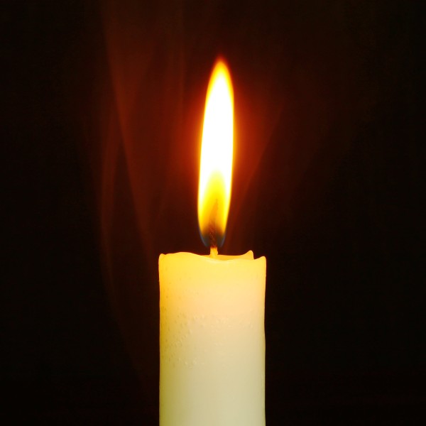 A lit candle infront of a dark background.