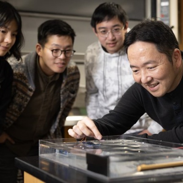 Three men and a woman gather around a robot demonstration in a laboratory.