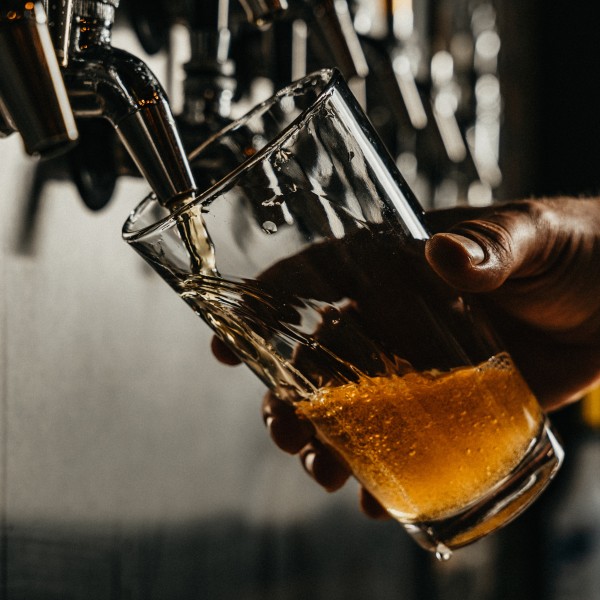 A hand pouring a glass of beer from a bar tap.