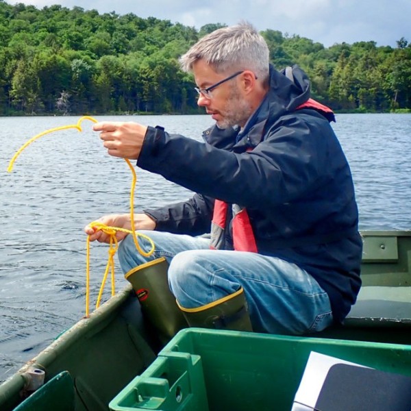 Stephen Jane sits in a boat deploys a sensor in an Adirondack lake